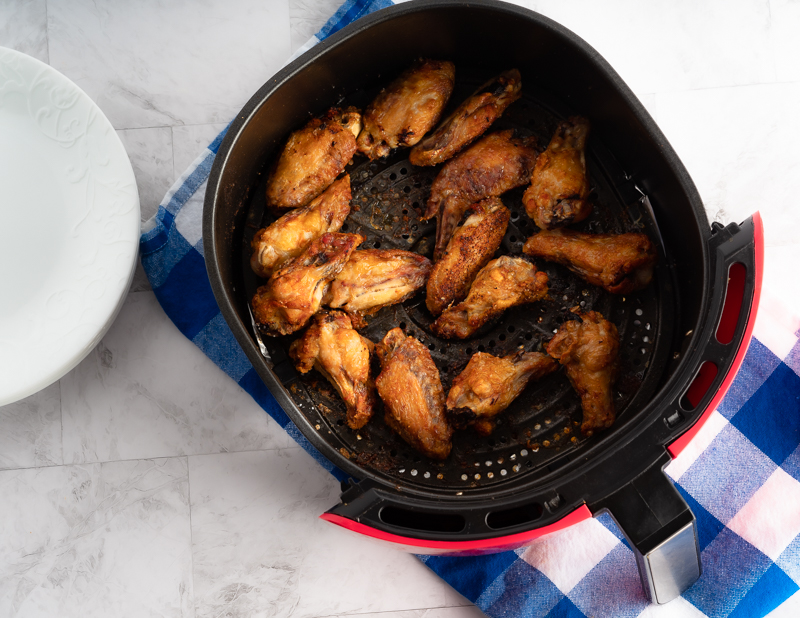 Air fryer chicken wings in a air fryer basket on top of a blue checkered napkin