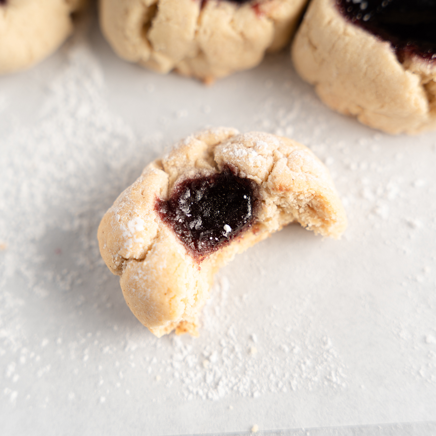Bite shot of a almond flour thumbprint cookie with a deep purple jam filling. 