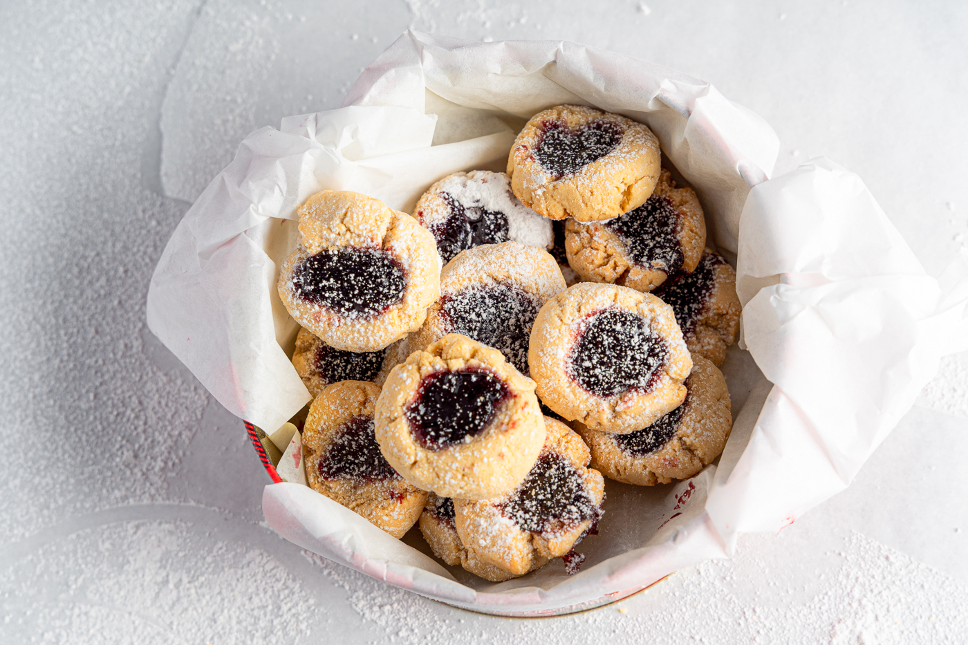 Almond Flour Thumbprint cookies in a cookie tin with powdered sugar
