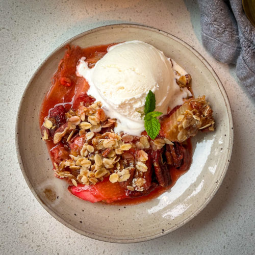 A small plate with strawberry rhubarb crisp and a scoop of vanilla ice cream melting over the hot dessert