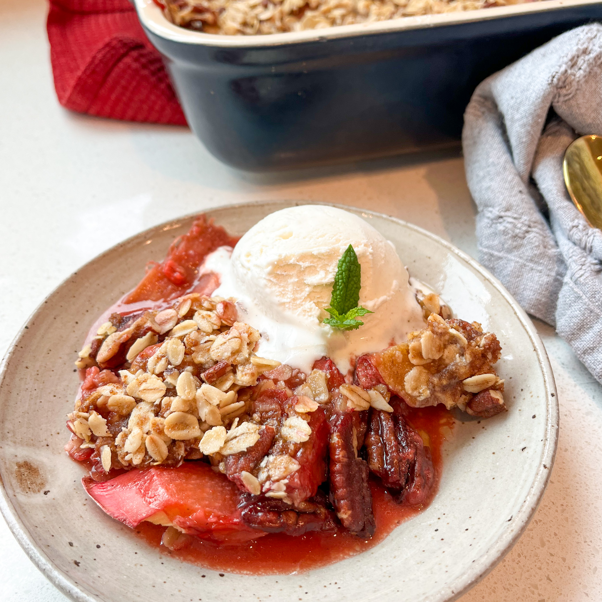 Strawberry Rhubarb Crisp on a stoneware plate with a scoop of ice cream and a garnish of mint