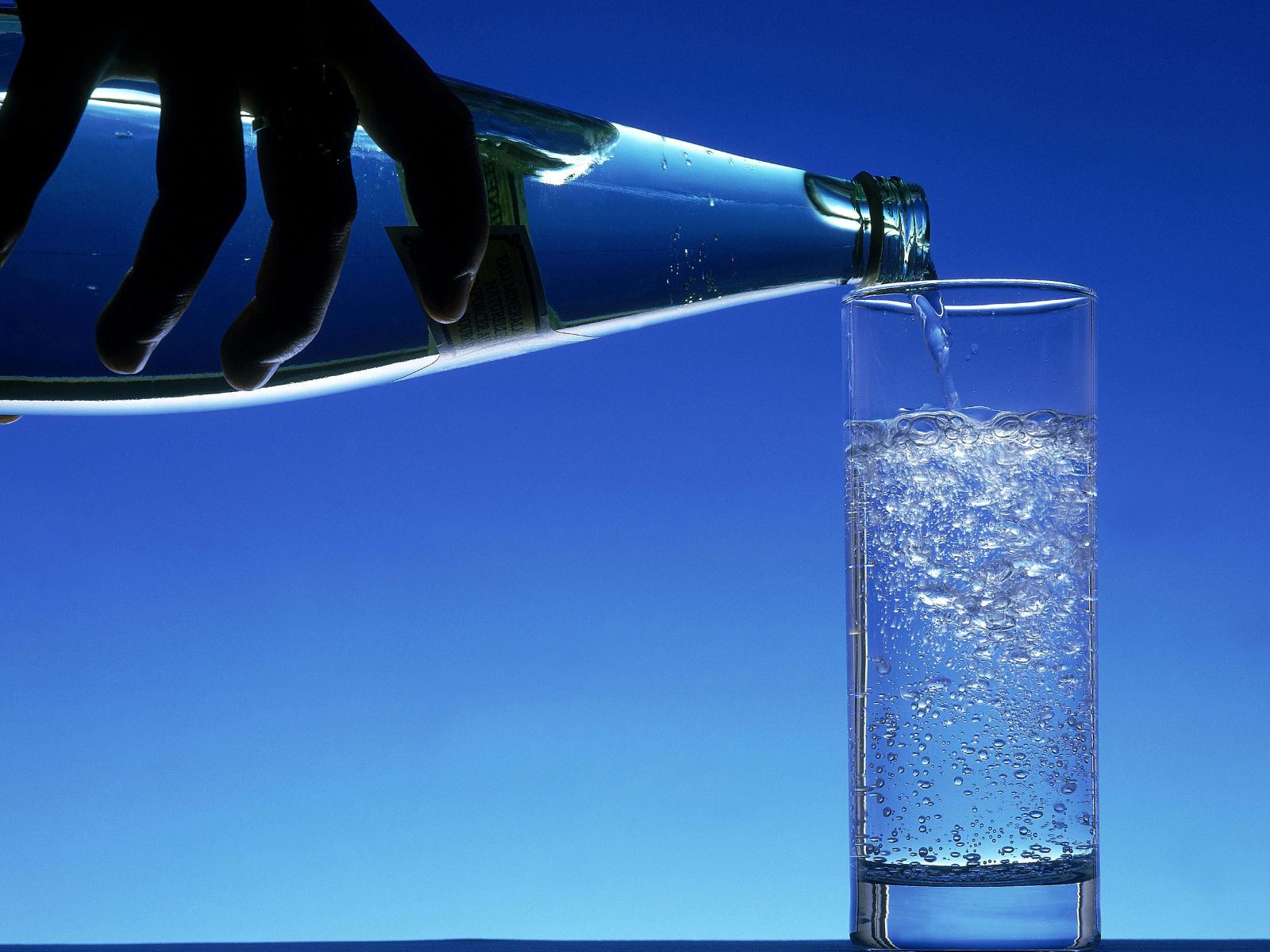 A bottle of mineral or sparkling water being poured into a tall glass. 