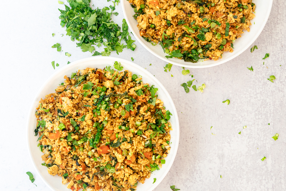 vegan tofu fried rice in two white bowls garnished with fresh herbs