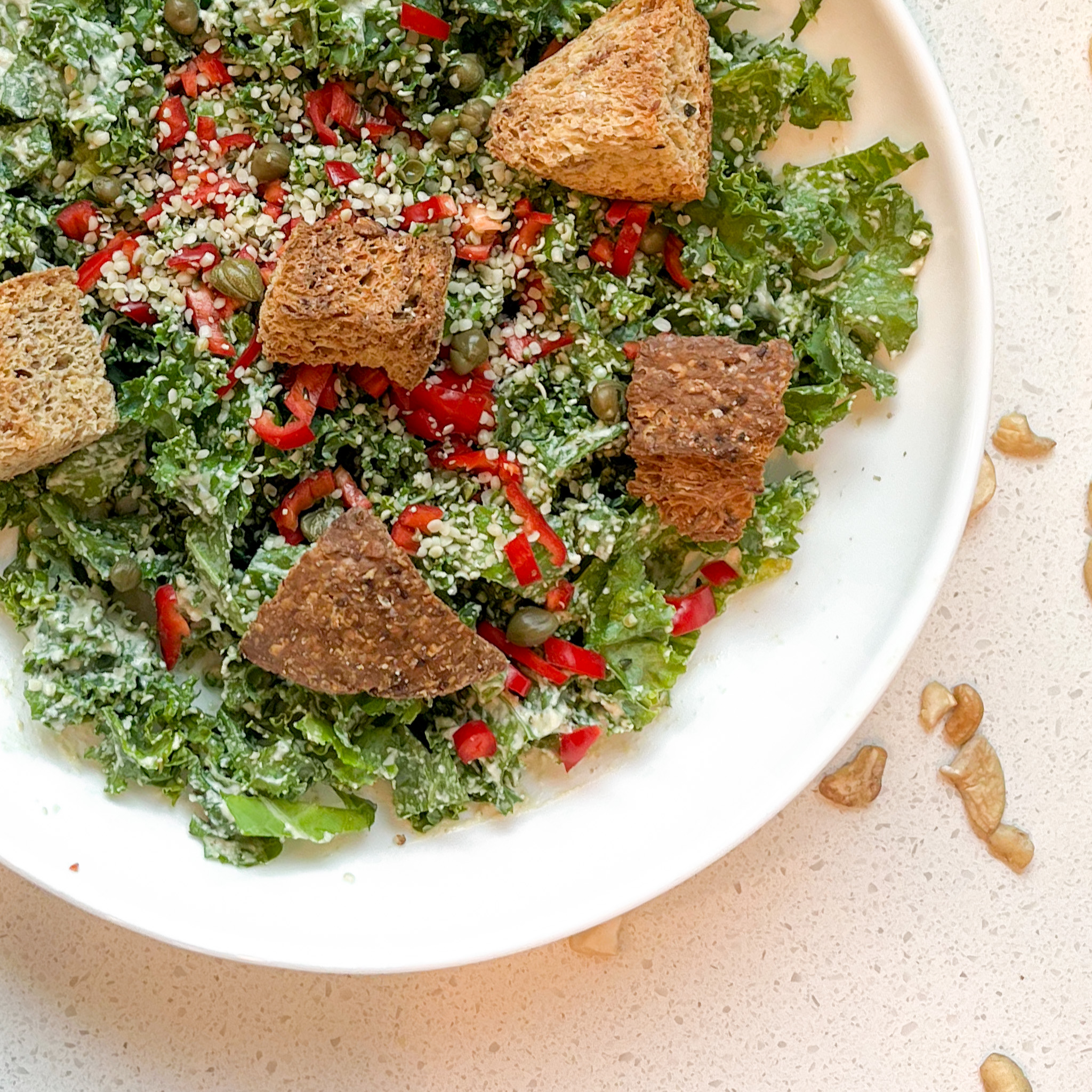 Kale caesar croutons, peppers, capers, hemp hearts in a white bowl