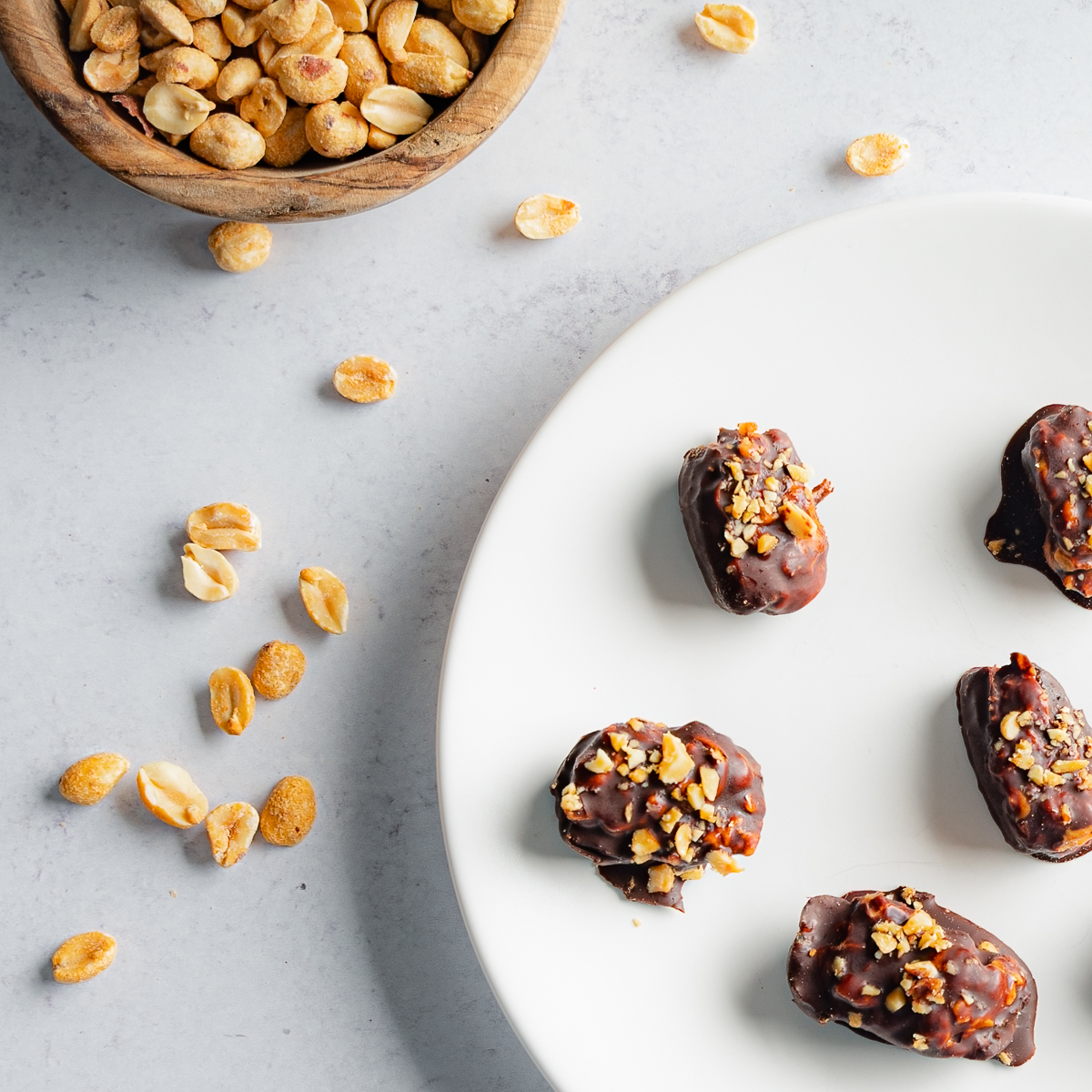 Close up of Dates Stuffed with Peanut Butter with peanuts scattered to the left and a bowl of peanuts in the top left corner