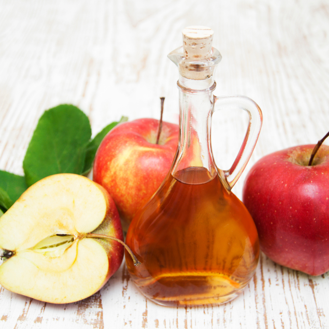 Image of Apple Cider Vinegar in a glass carafe with red apples around it. 