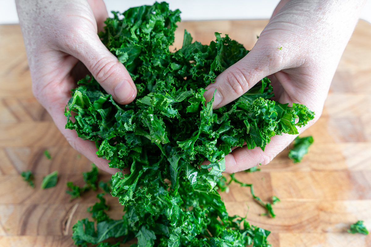 Vibrant green kale that has been chopped, gathered between two hands over a cutting board