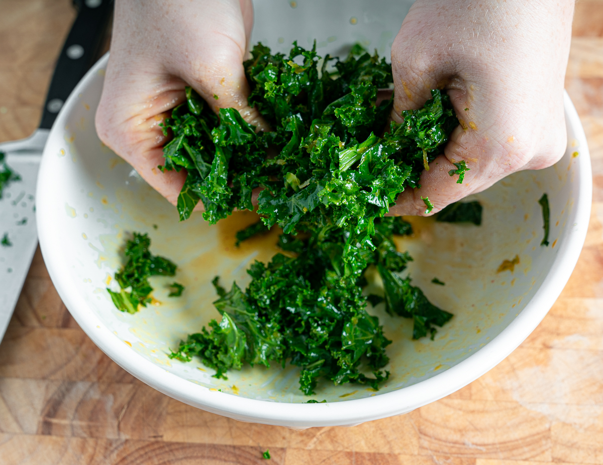 massaging bright green kale with hands in a white bowl