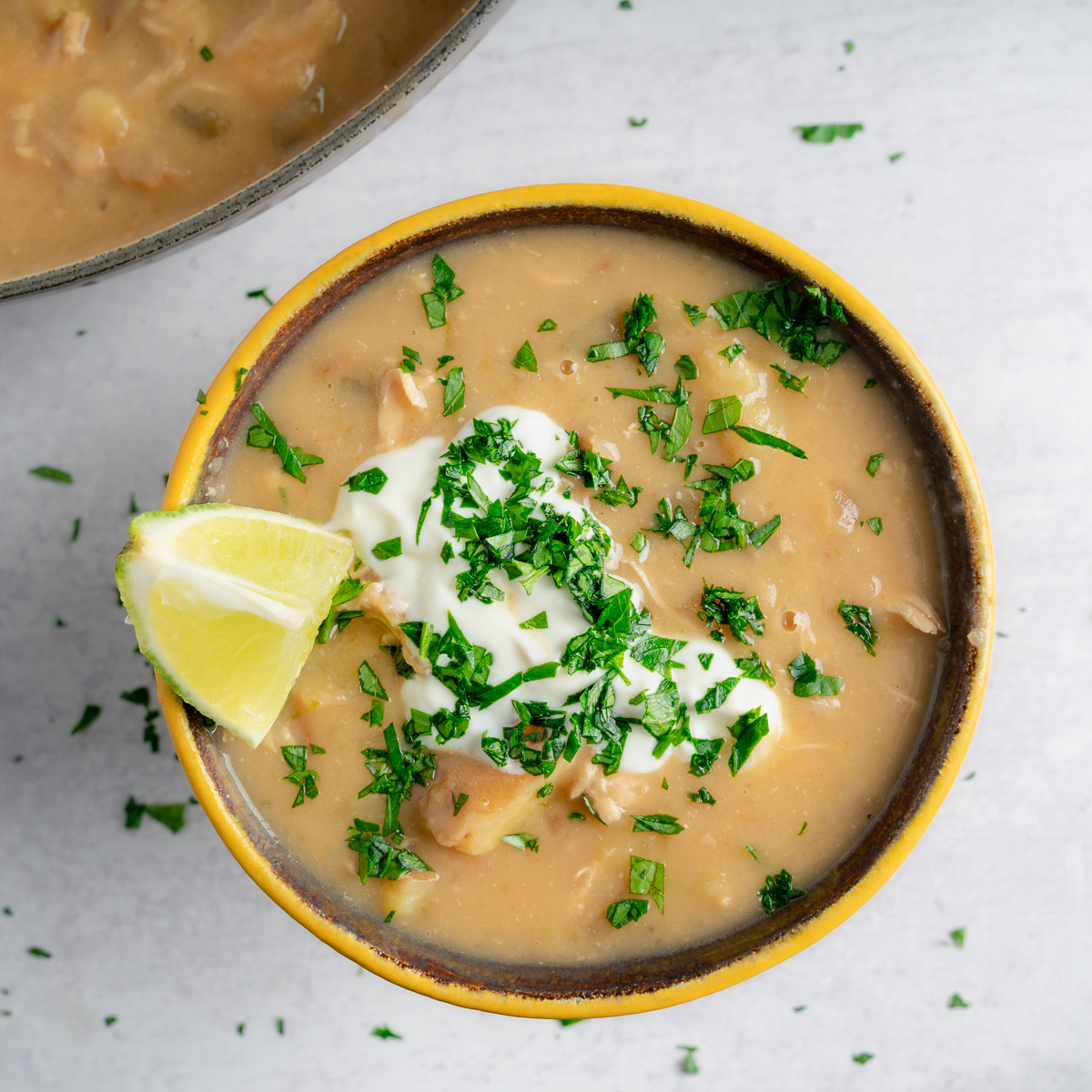 coconut lime chicken chowder in bowl with a lime wedge, a cream sauce, and minced herbs