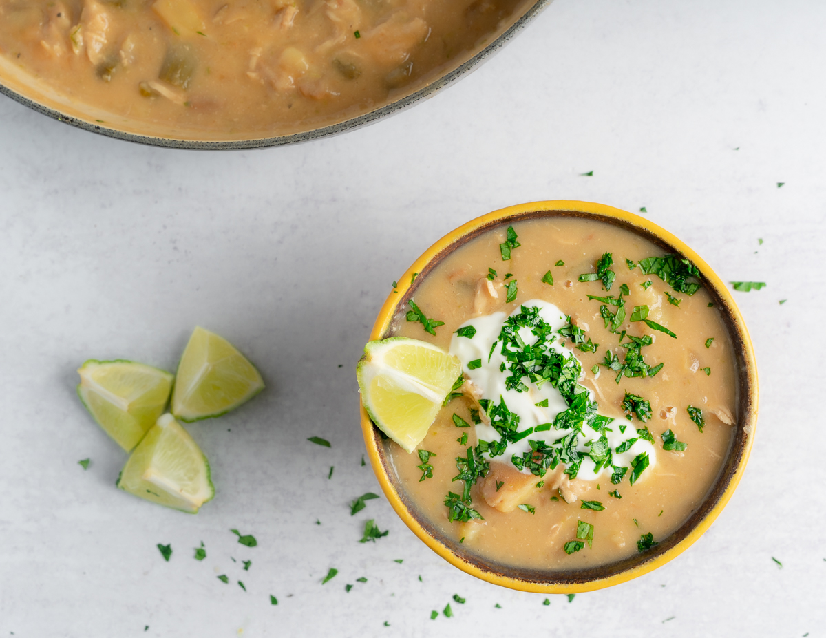 coconut lime chicken chowder with lime wedge in bowl with a soup pot in the top left corner
