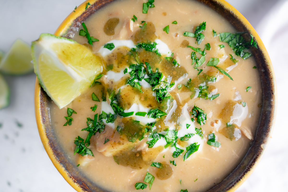 close up coconut lime chicken chowder with lime, minced herbs, and a green hot sauce drizzle