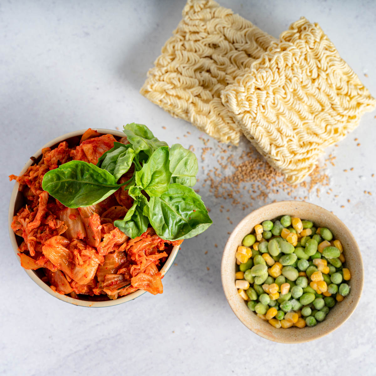 vegan-kimchi-instant-ramen-ingredients including red kimchi with basil, 2 ramen noodle blocks, and frozen peas and corn. 