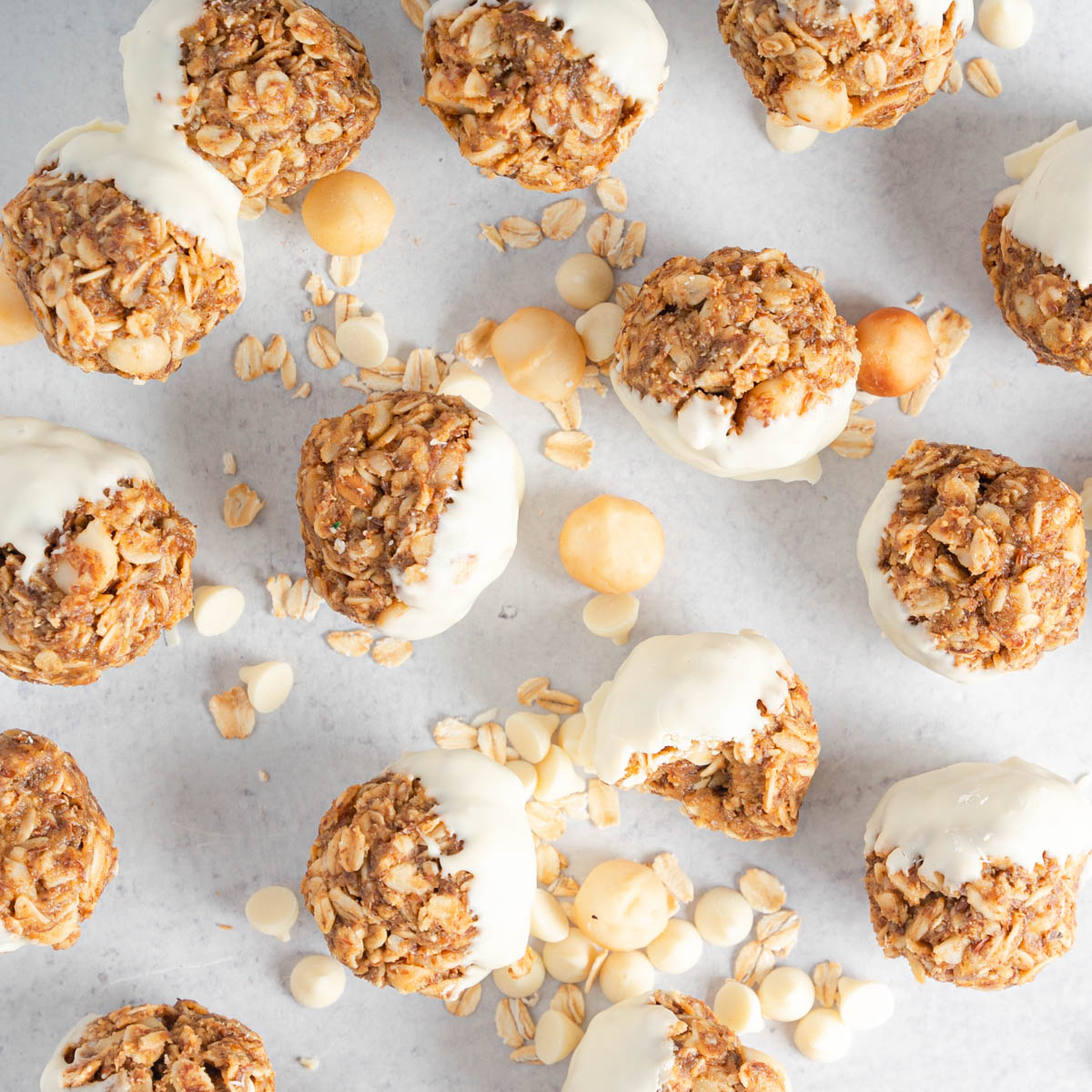 Top down of many white chocolate macadamia nut bites. Noted macadamia nut and oat bites scattered over off white background.