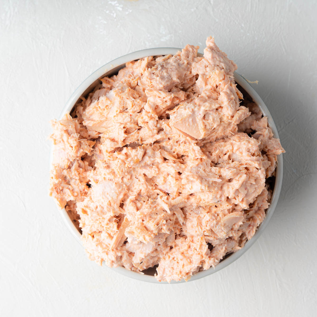 Spicy canned tuna with creamy mayo and siracha making the mixture a pink-ish hue, mixed and displayed in a bowl.