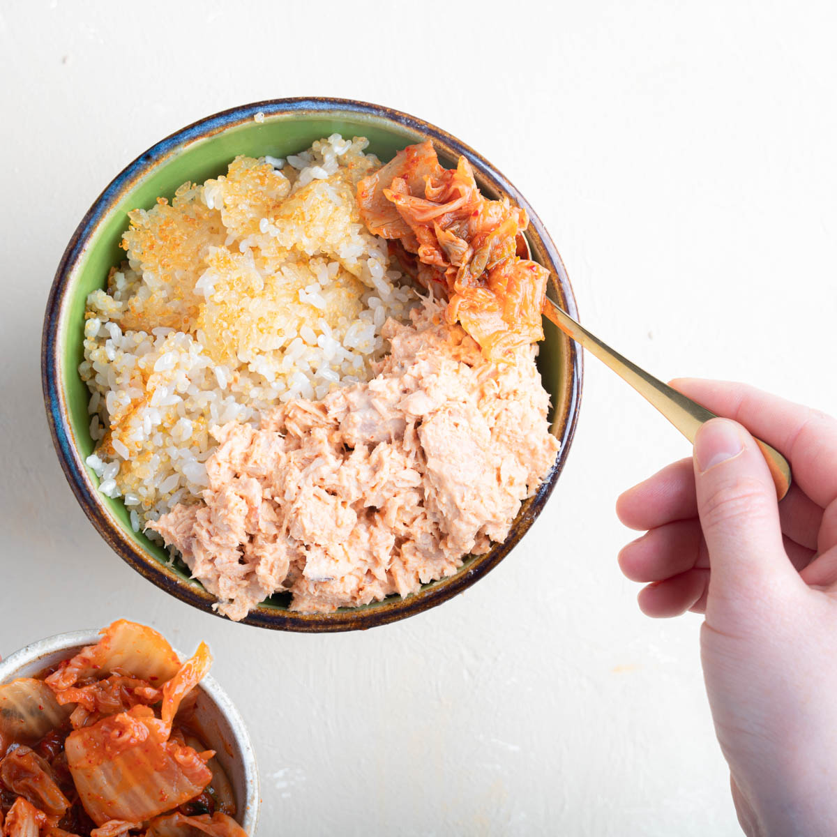 Spooning Kimchi over a bowl of crispy rice and spicy tuna