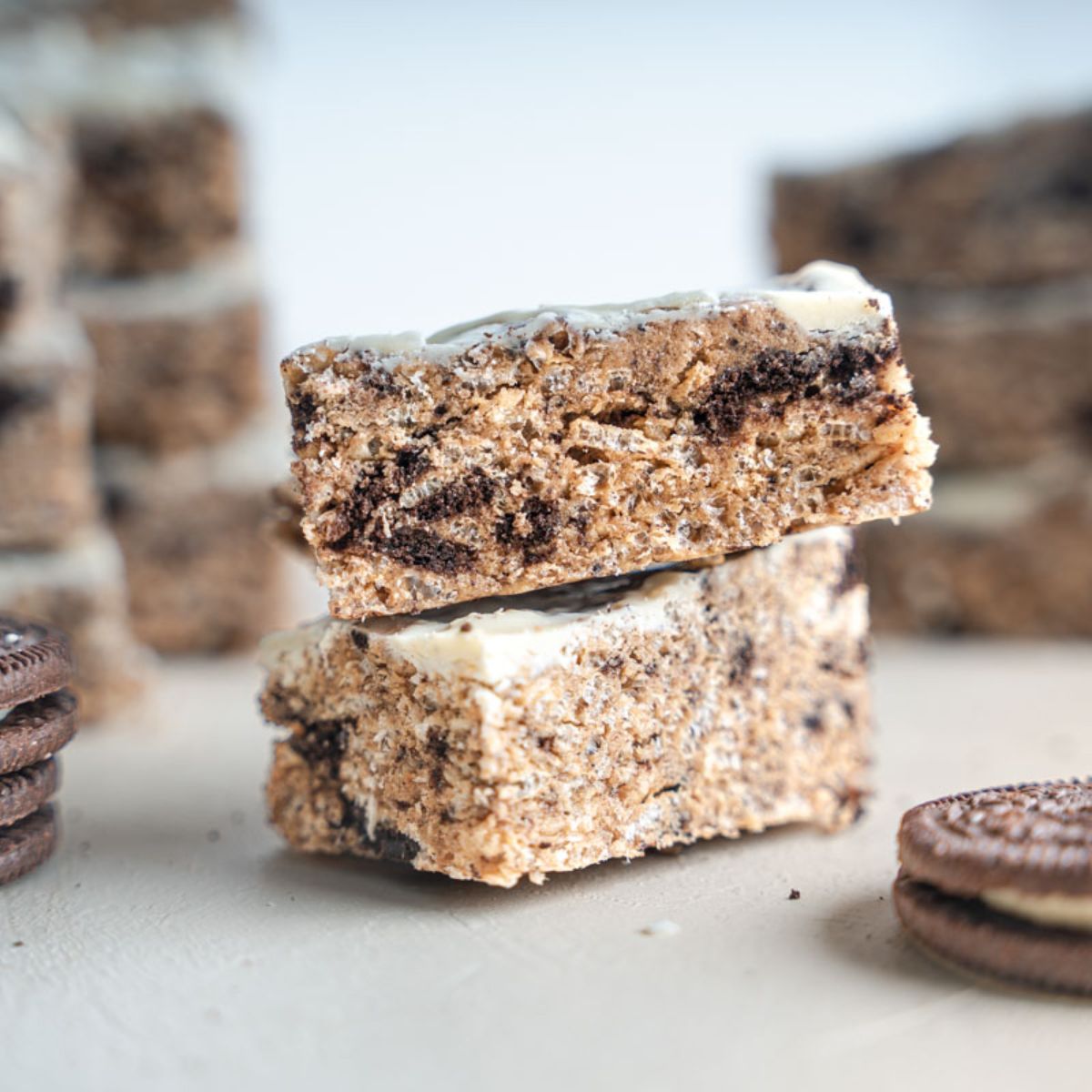 Two Cookies and Cream Protein Bars stacked with oreos and other bars in the back and foreground