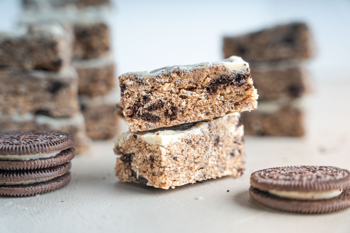 Two cookies and cream crunch bars stacked. With oreos scattered around them.