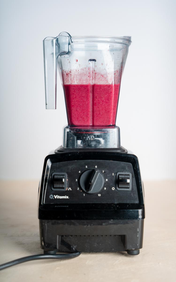 A blender with a bright purple berry rhubarb smoothie in it just after blending