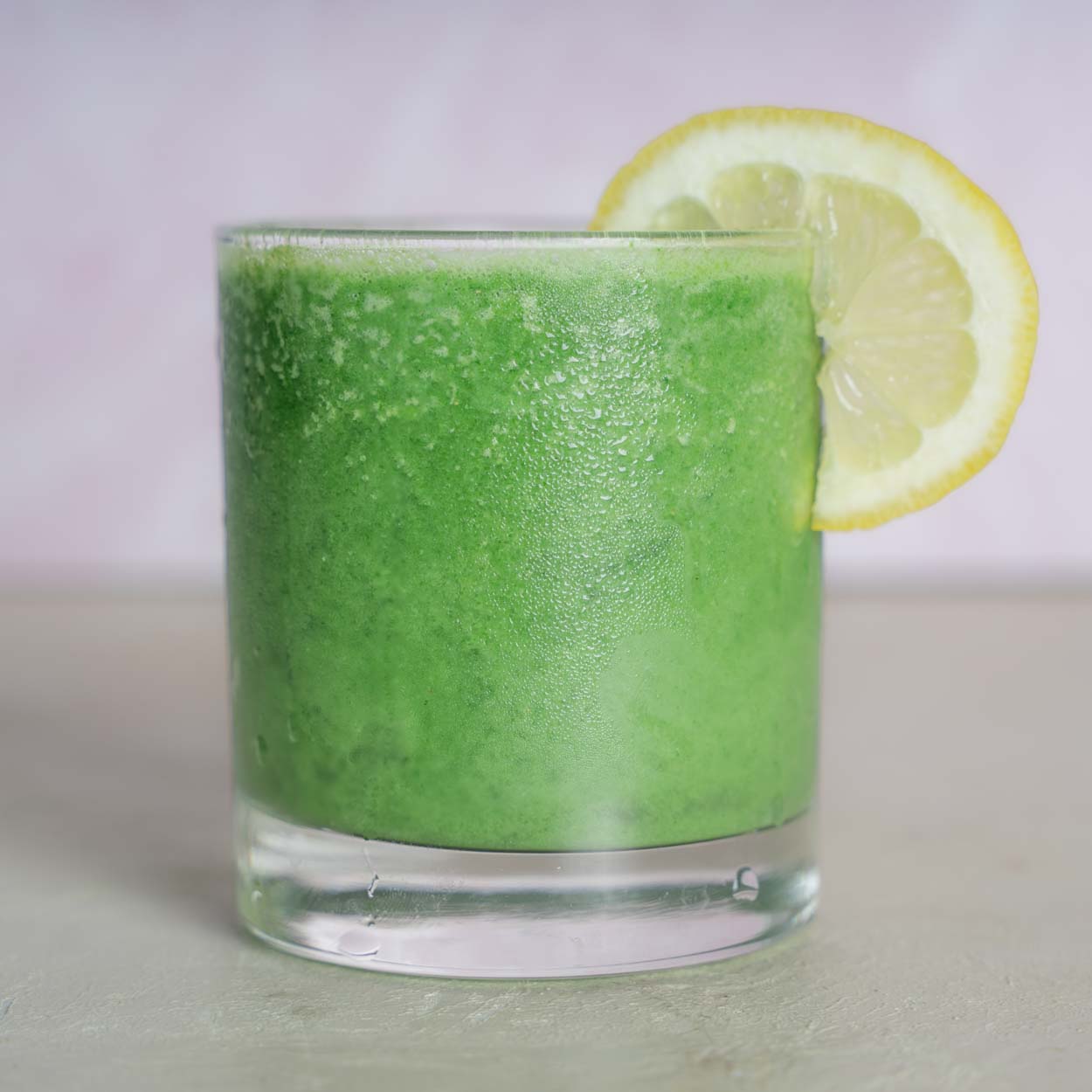 Green juice smoothie in a small juice glass garnished with a lemon slice. 