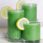 Green juice smoothie in three different sized glasses garnished with lemon
