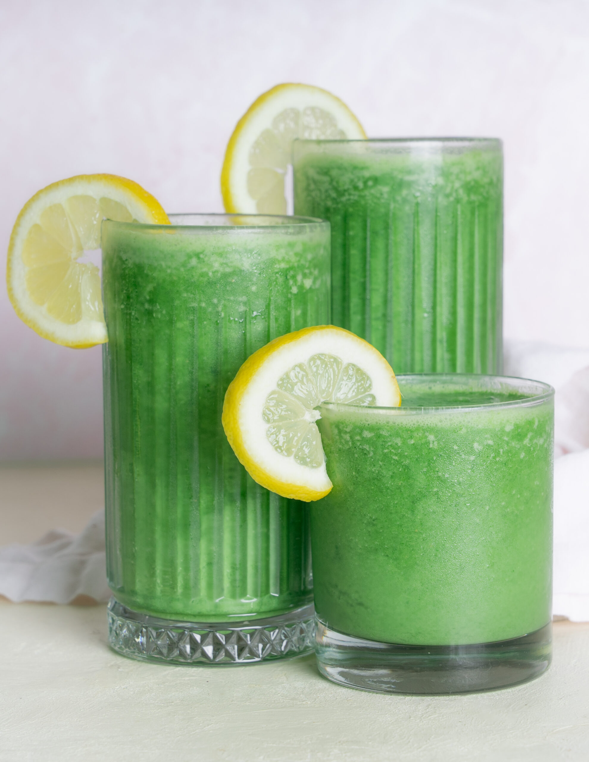 Green juice smoothie in three different sized glasses garnished with lemon