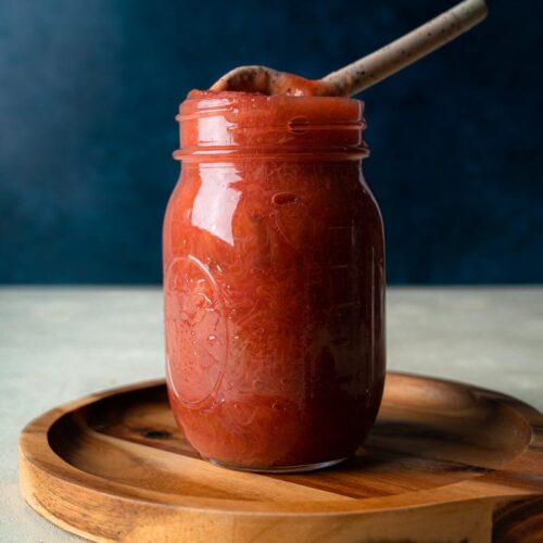 Redish-Pink Rhubarb compote in a 10oz mason jar with a spoon dipped into the top