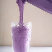 Berry Bliss Smoothie being poured into a decorative glass. The glass is almost completely full. The color of the smoothie is purple-blueish.