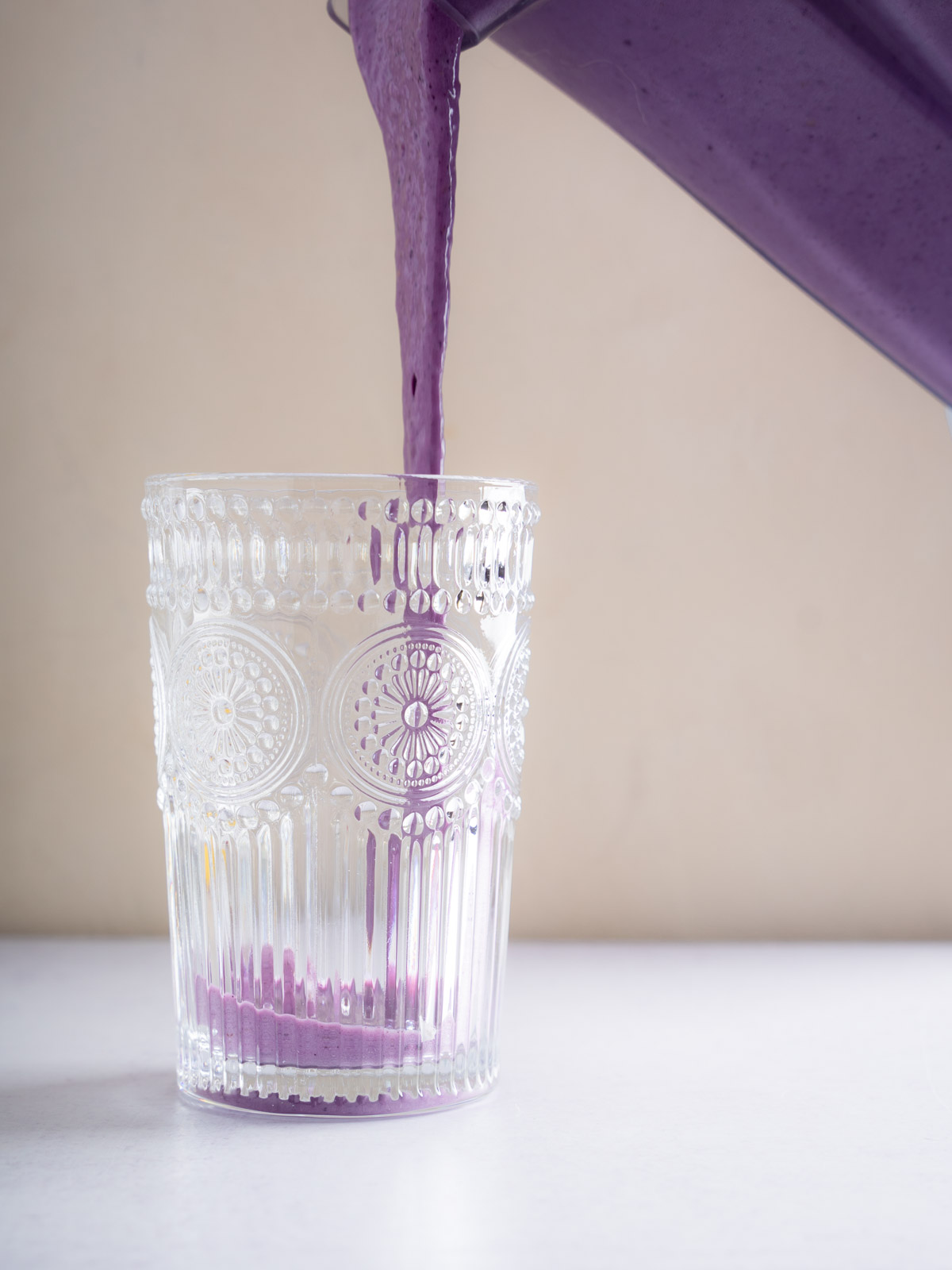Berry Bliss Smoothie being poured into a decorative glass from a blender. The Berry Blast Smoothie is creamy, with a blue-purple color.