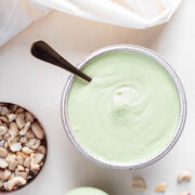 Light green cilantro cashew dressing in a bowl next to a bowl of cashews.