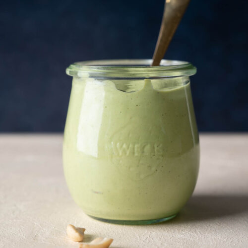 A glass container full of a light green cilantro cashew dressing.