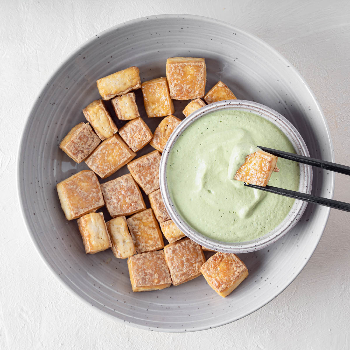 Creamy light green cilantro cashew dressing is sitting in a large bowl with crispy tofu.