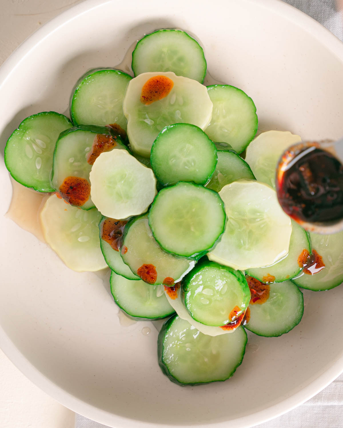 Din Tai Fung Cucumber Salad recipe plated and a chili oil crisp being drizzled over top with a small spoon. 