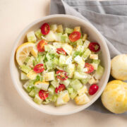 A top down view of lemon cucumber salad with sliced tomatoes, diced cucumbers, and green onion. A lemon wedge is to the left in the bowl.