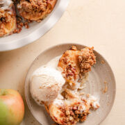 A grey speckled dessert plate with 2 halves of baked apples with pecan oat topping and a scoop of creamy ice cream and a bite taken from the plate.