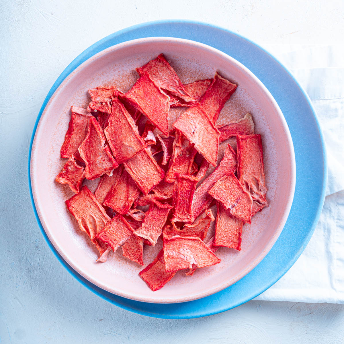 Top down view of dehydrated watermelon on a pink plate over a larger blue plate. 