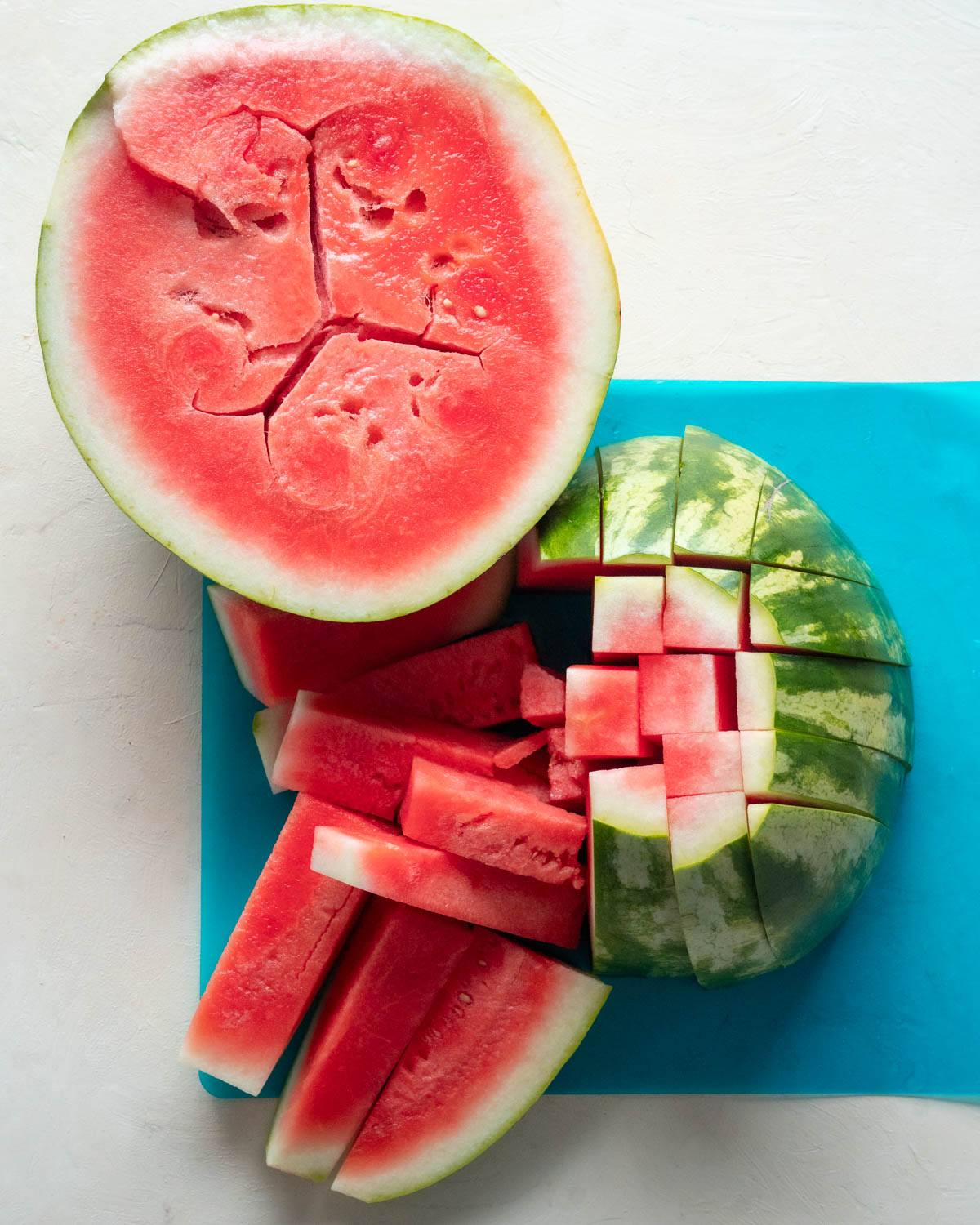Top down view of fresh watermelon over a off white background and a blue plastic cutting board. 
