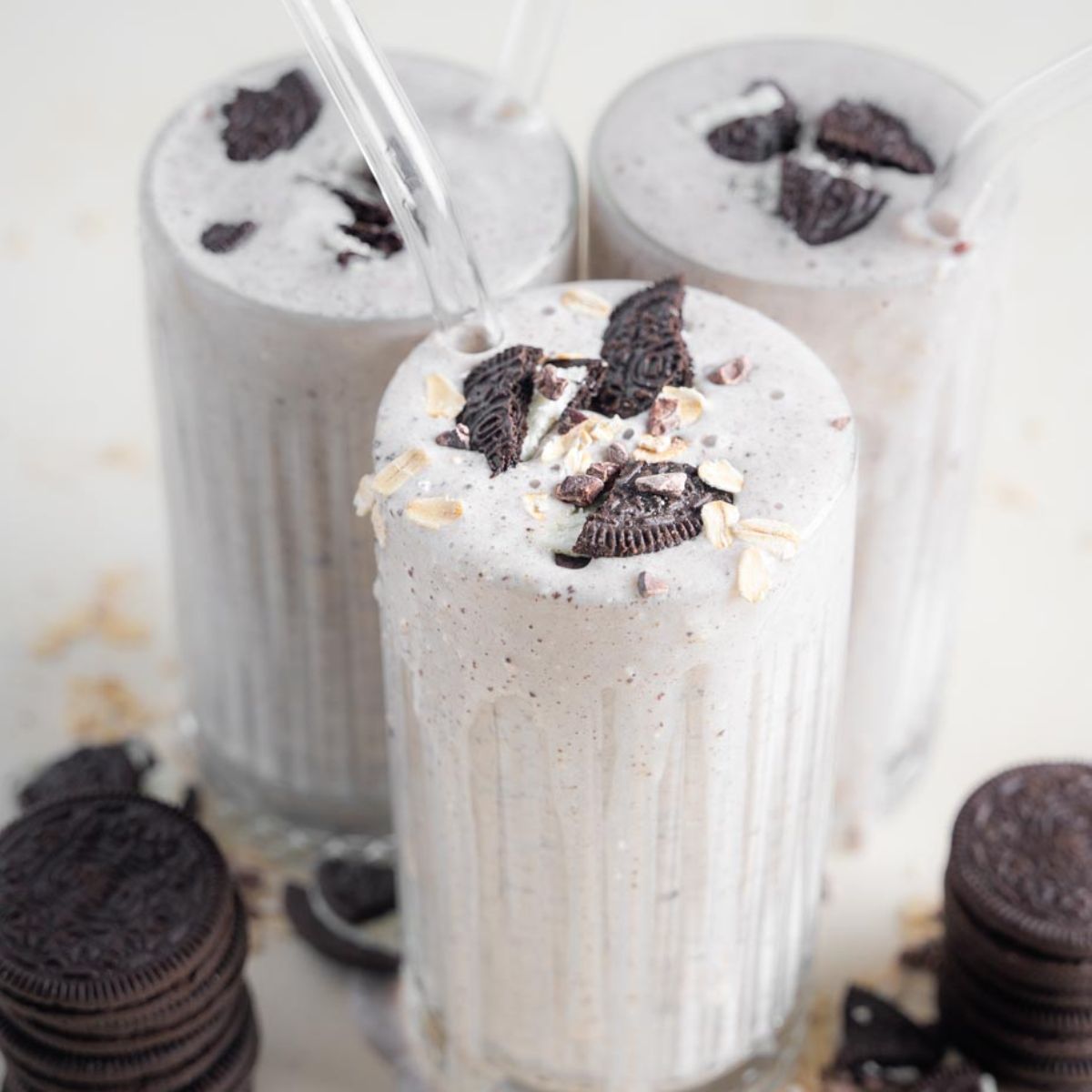 Oreo Milkshake without Ice Cream three glasses with straws and crushed oreos over top. Oreos surrounding the glasses. 