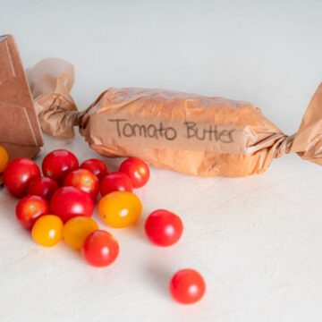 tomato butter wrapped in parchment paper with spilled yellow and red cherry tomatoes to the left