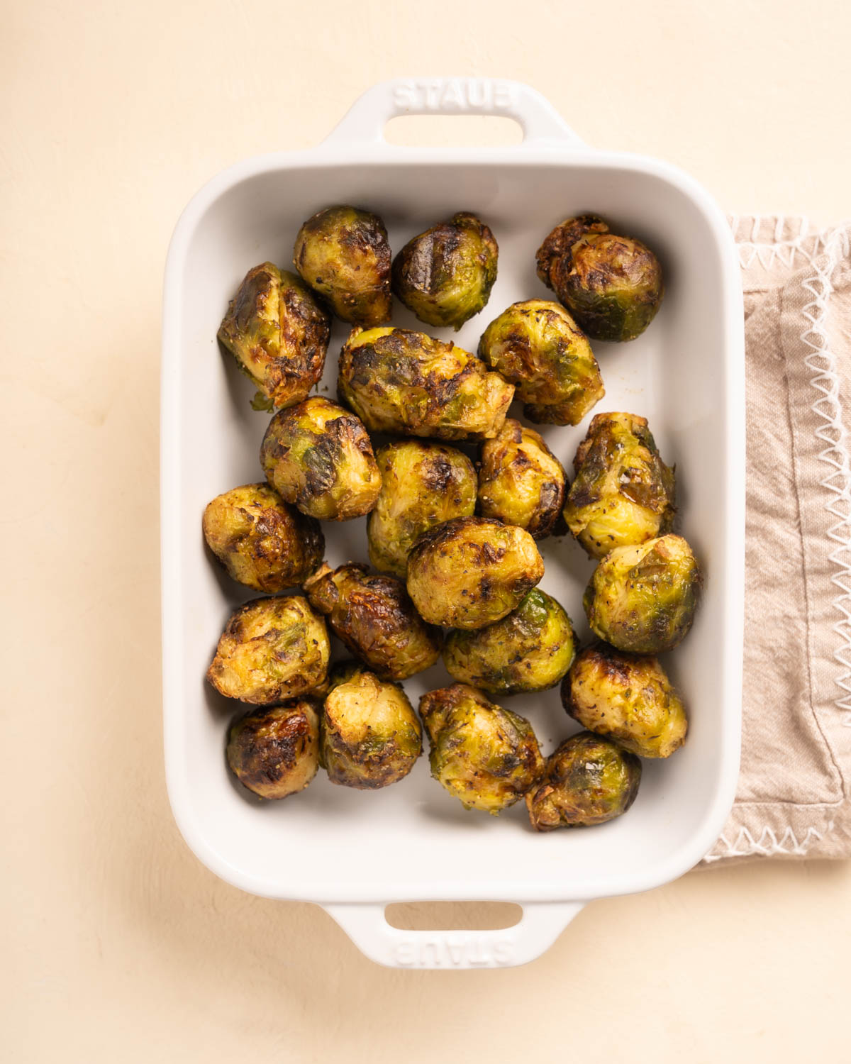 Golden Brown Air Fryer Brussels Sprouts in a white baking dish over a cream colored background. 