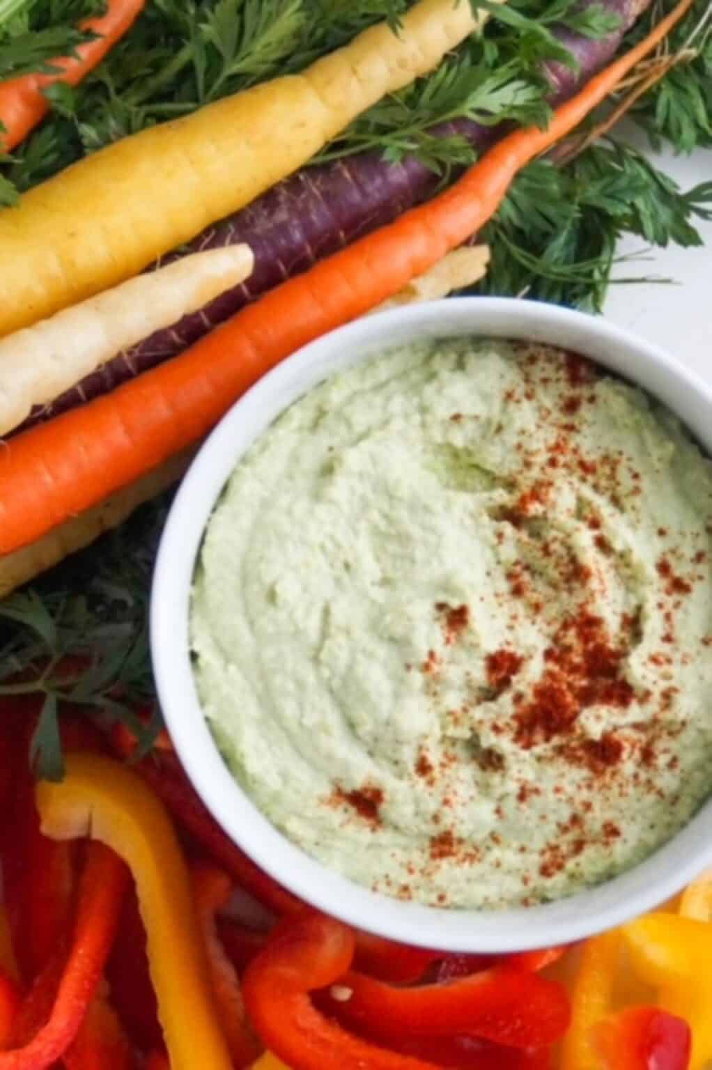 Edamame Hummus in a white bowl garnished with red paprika against the green creamy dip. 