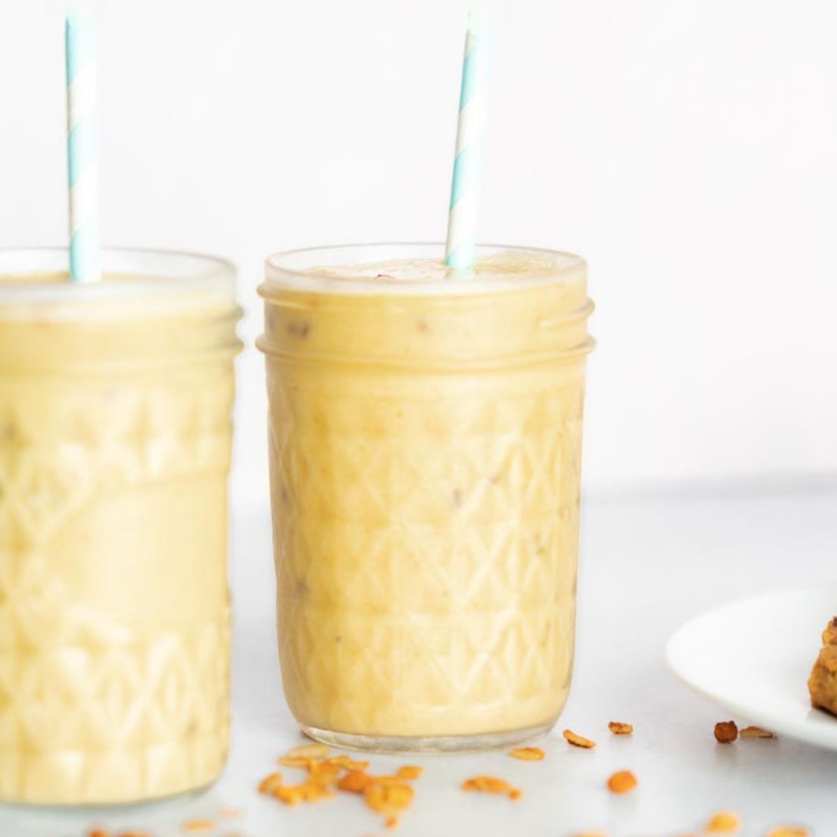 Two 8oz mason jars with straws with toasted oats scattered on the table. 
