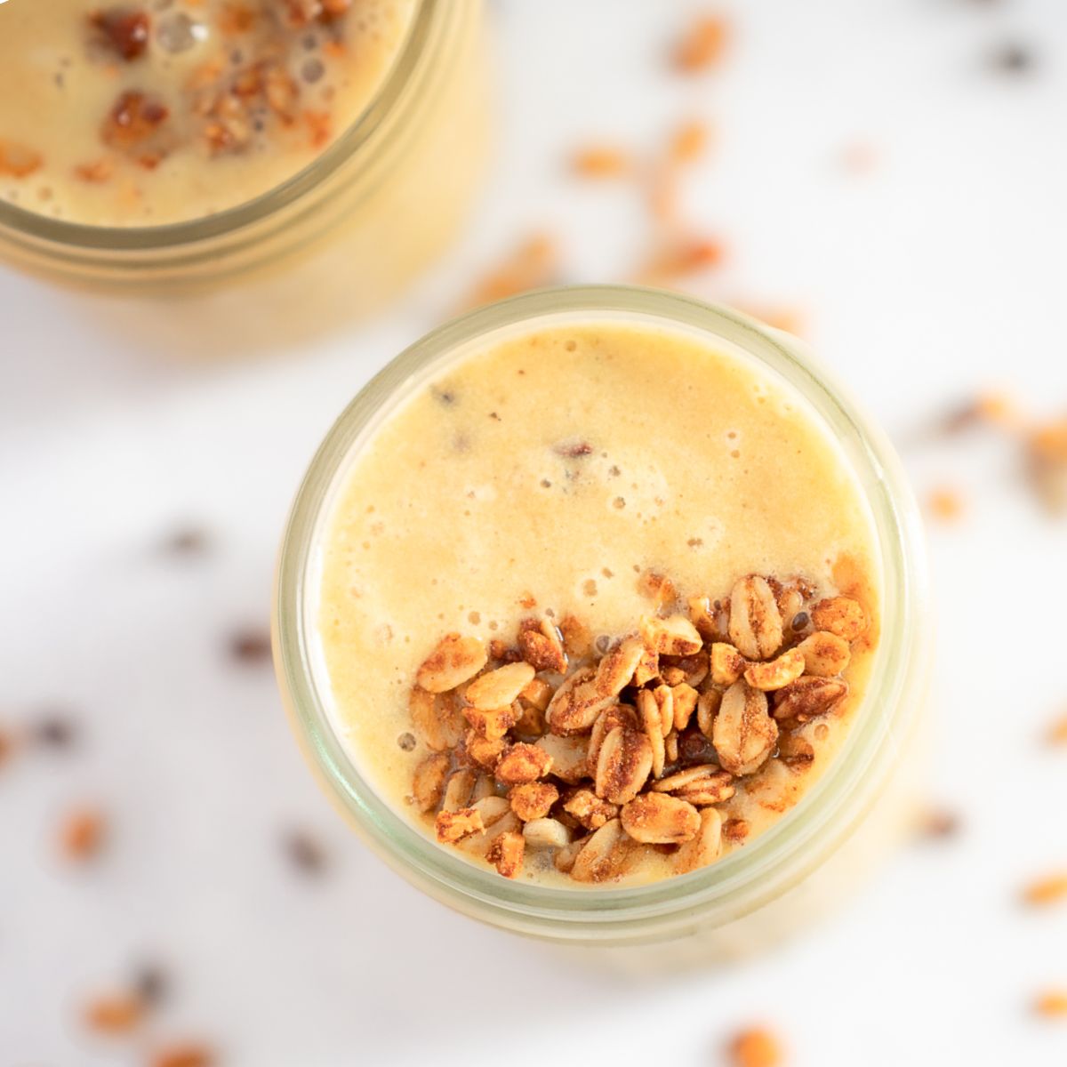 Close up of a pumpkin smoothie with chestnuts. Toasted oats are scattered on the table and overtop the light orange smoothie. 