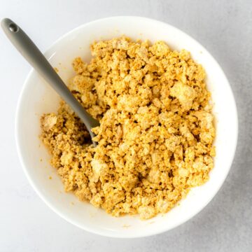 Tofu Scramble with a grey serving spoon dipped into the white bowl with golden yellow tofu crumbles.