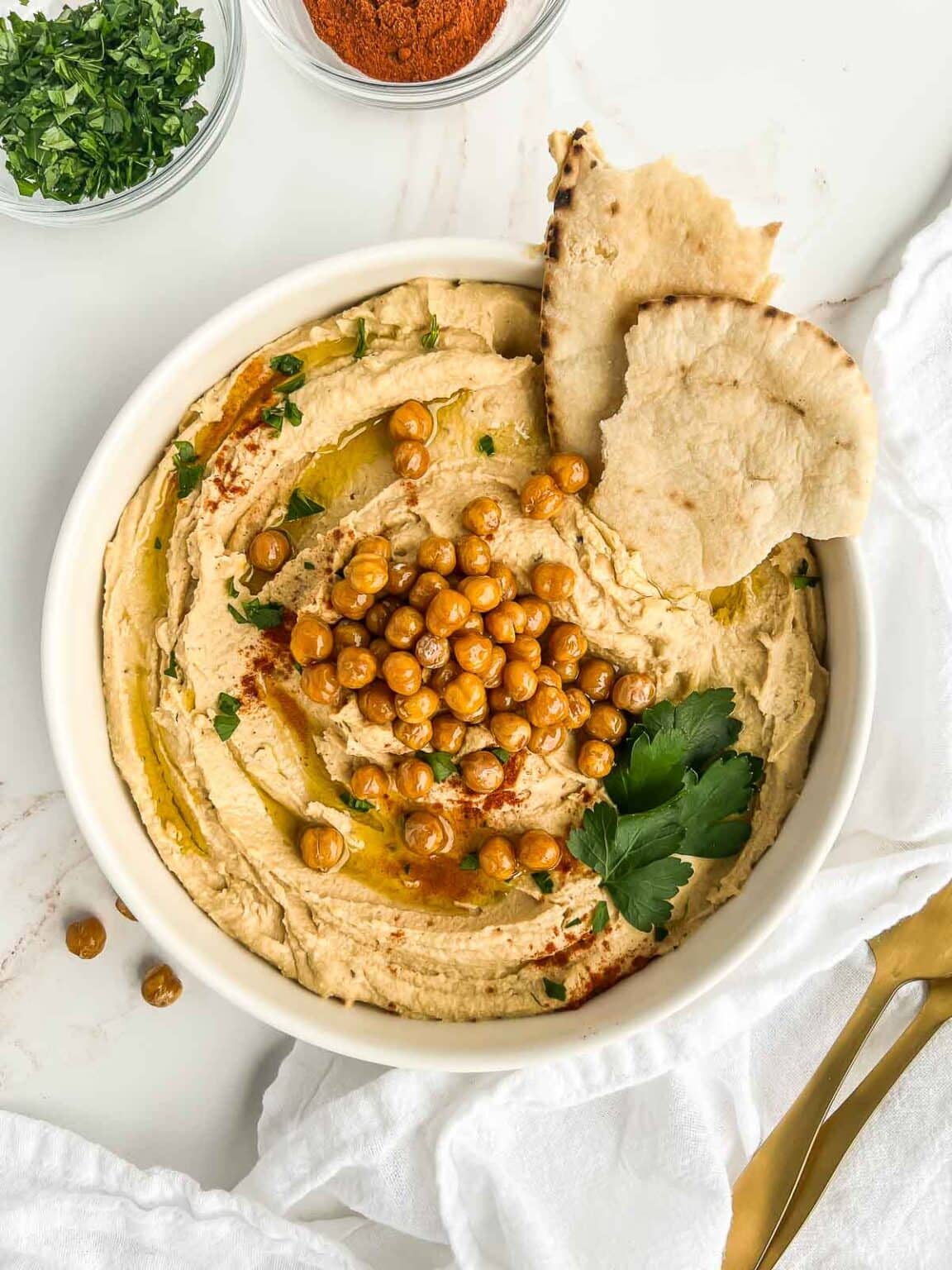 Garlic Free Hummus in a white bowl topped with toasted chickpeas and herbs. 