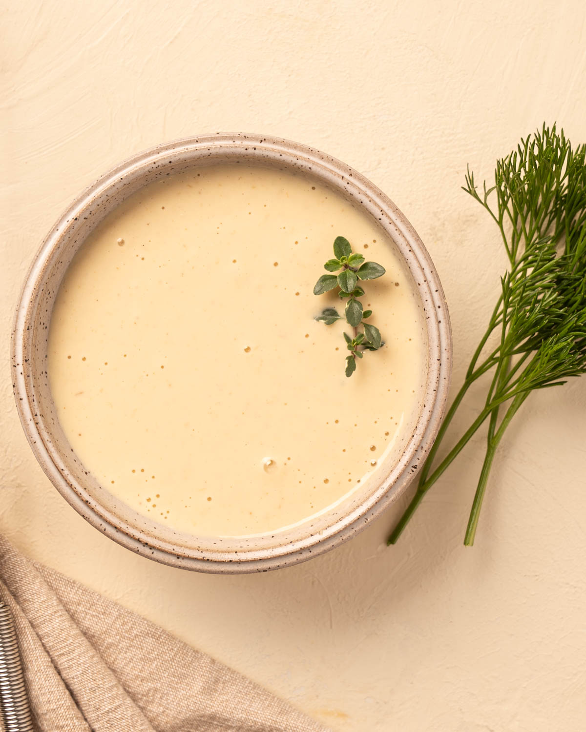 A stoneware bowl with a cream Horseradish Aioli along side some bright herbs.