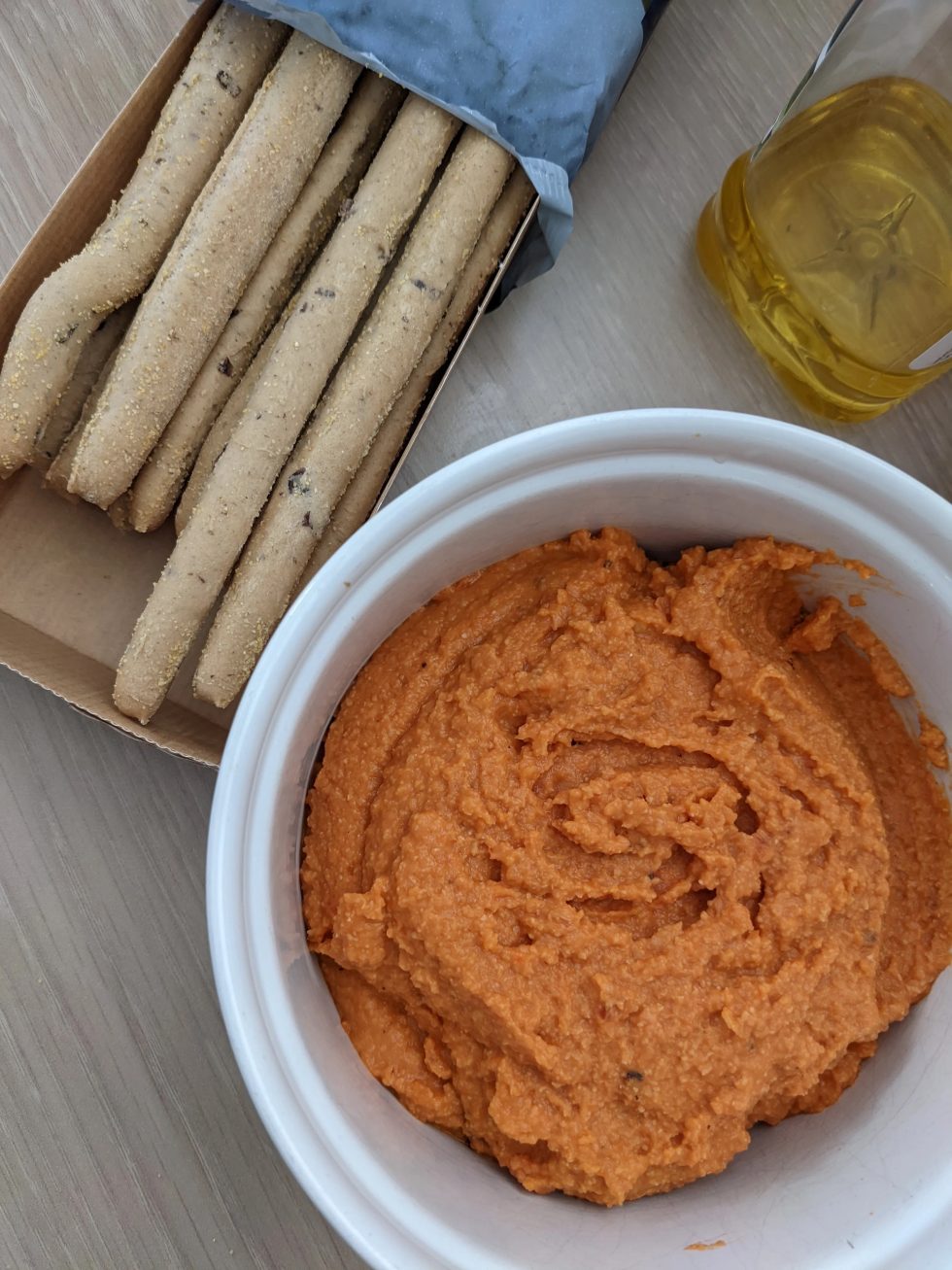 A White bowl filled with Tomato Pepper and Chickpea Dip to the left of the bowl is a bow filled with seeded cracker straws. 