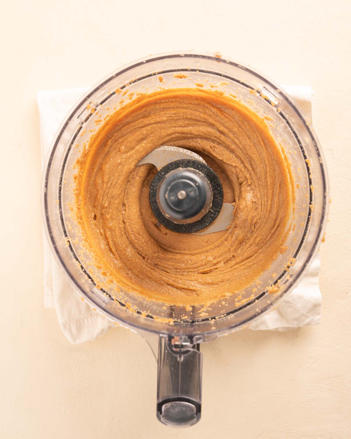 A food processor after the peanuts, maple syrup, vanilla, and cinnamon have been blended into a smooth butter