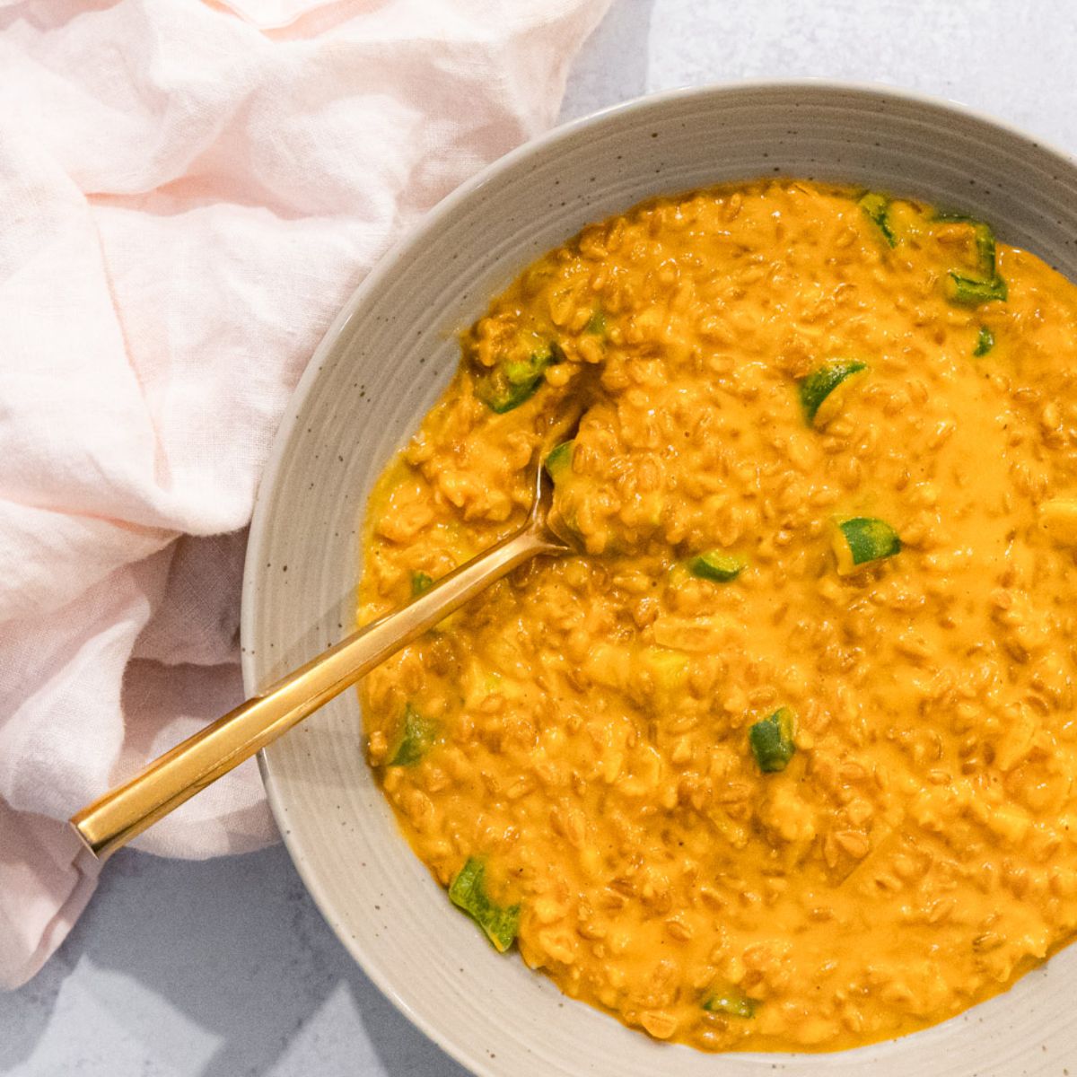 Bright orange-yellow Risotto in a stoneware bowl with a gold spoon