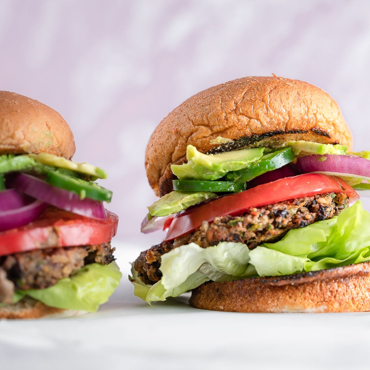 Two burgers with lettuce, tomato, onion, and jalapeno piled high.