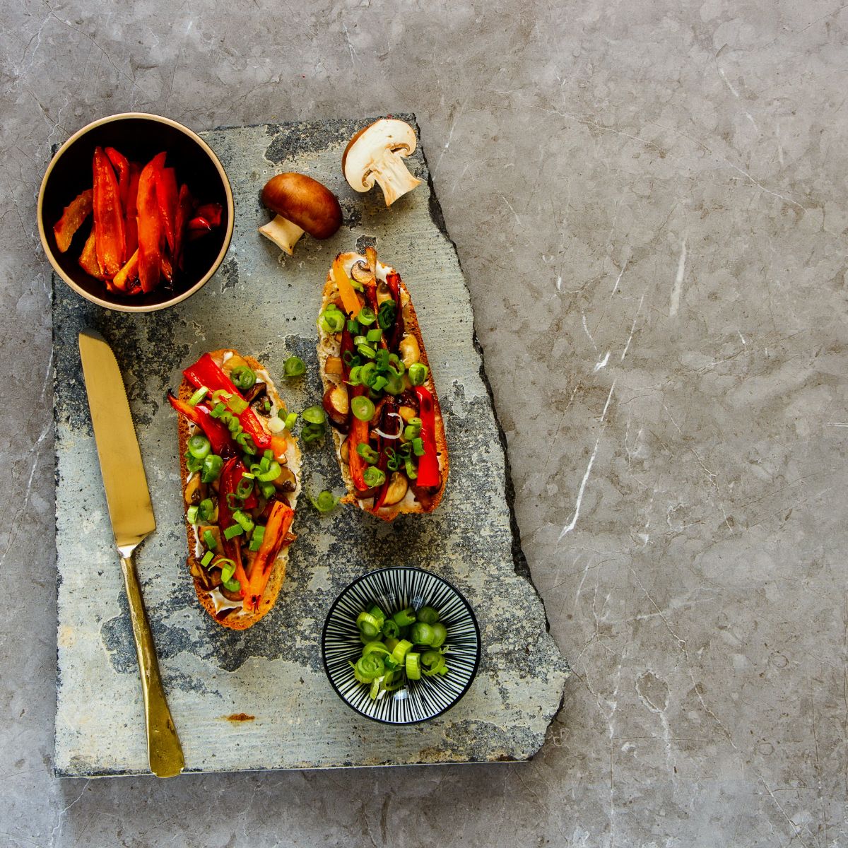 Mushroom Toast on a stone backdrop with small bowls filled with red peppers and green onion. 